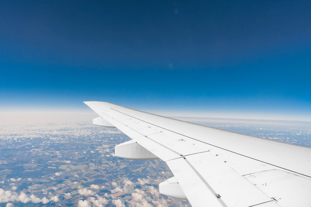 Asa de avião vista da janela, com céu azul e nuvens abaixo