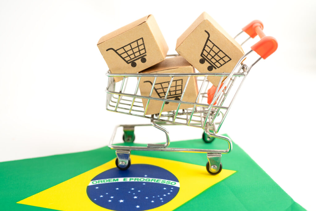 Carrinho de supermercado cheio de caixas de compras, em cima de uma bandeira do Brasil ilustra investimentos no varejo brasileiro.
