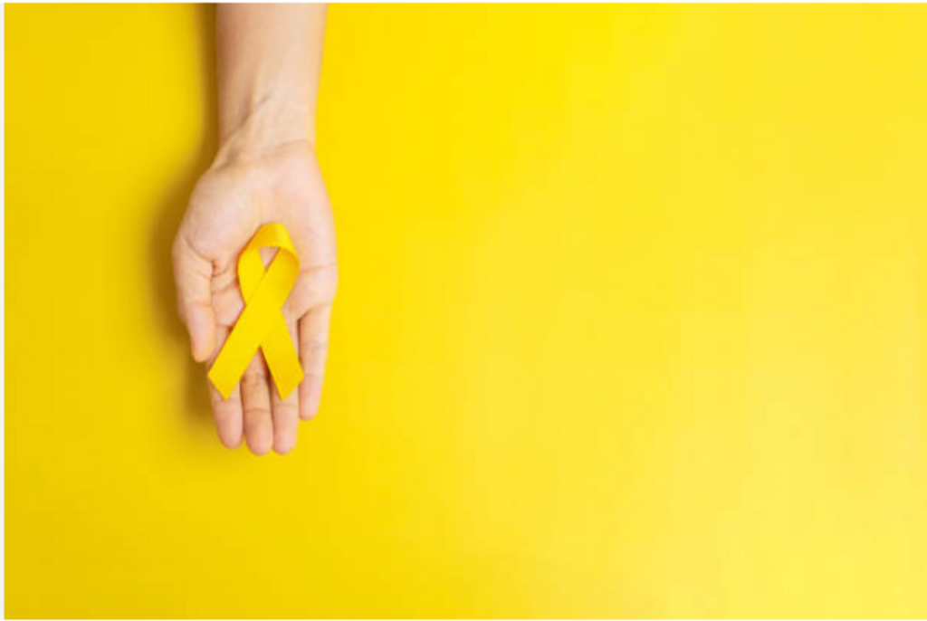 Mão segurando laço amarelo, em fundo amarelo