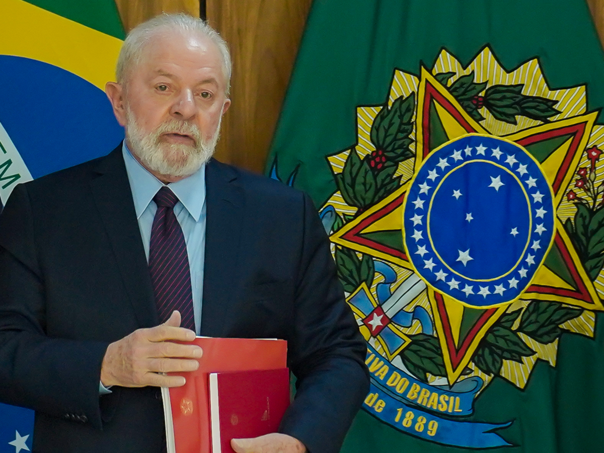 Lula com bandeiras ao fundo, de terno, segurando documentos