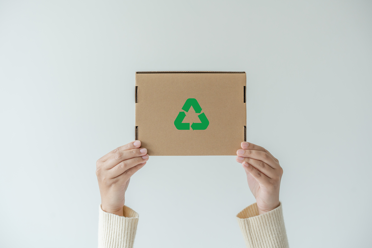 Mãos levantando uma caixa de papelão com símbolo verde de sustentabilidade