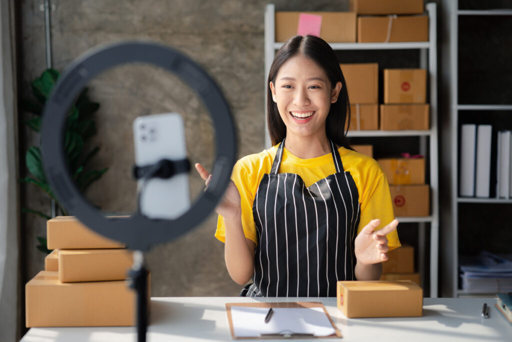 Mulher chinesa olhando para celular em ring light fazendo live shopping; pequenas empresas online; social commerce