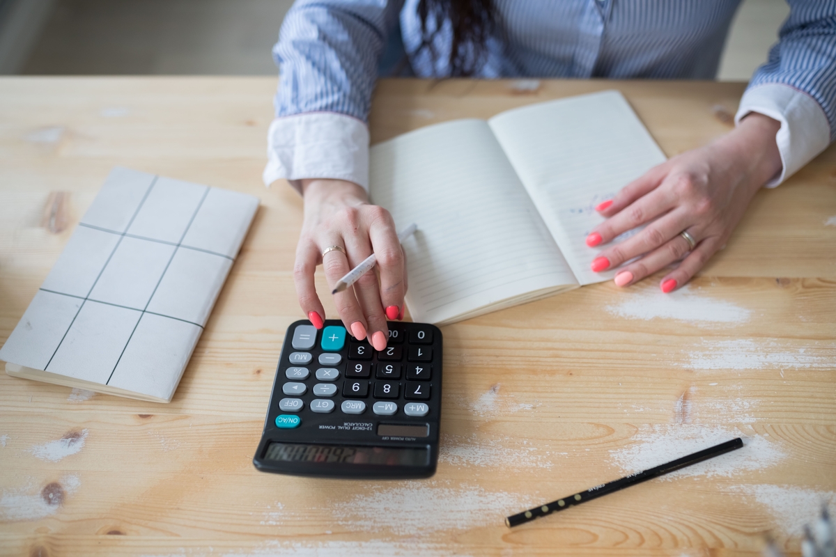 Mulher fazendo contas em calculadora e caderno