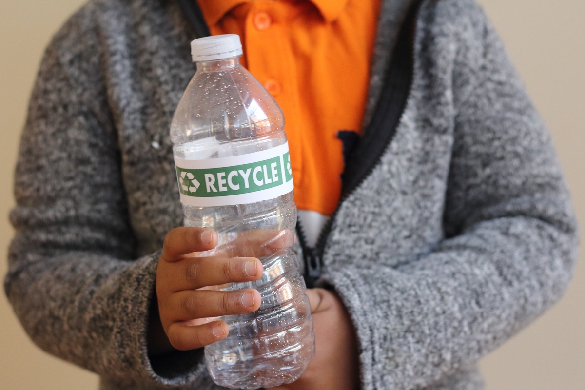 Pessoa com garrafa pet na mão com rótulo "recicle"
