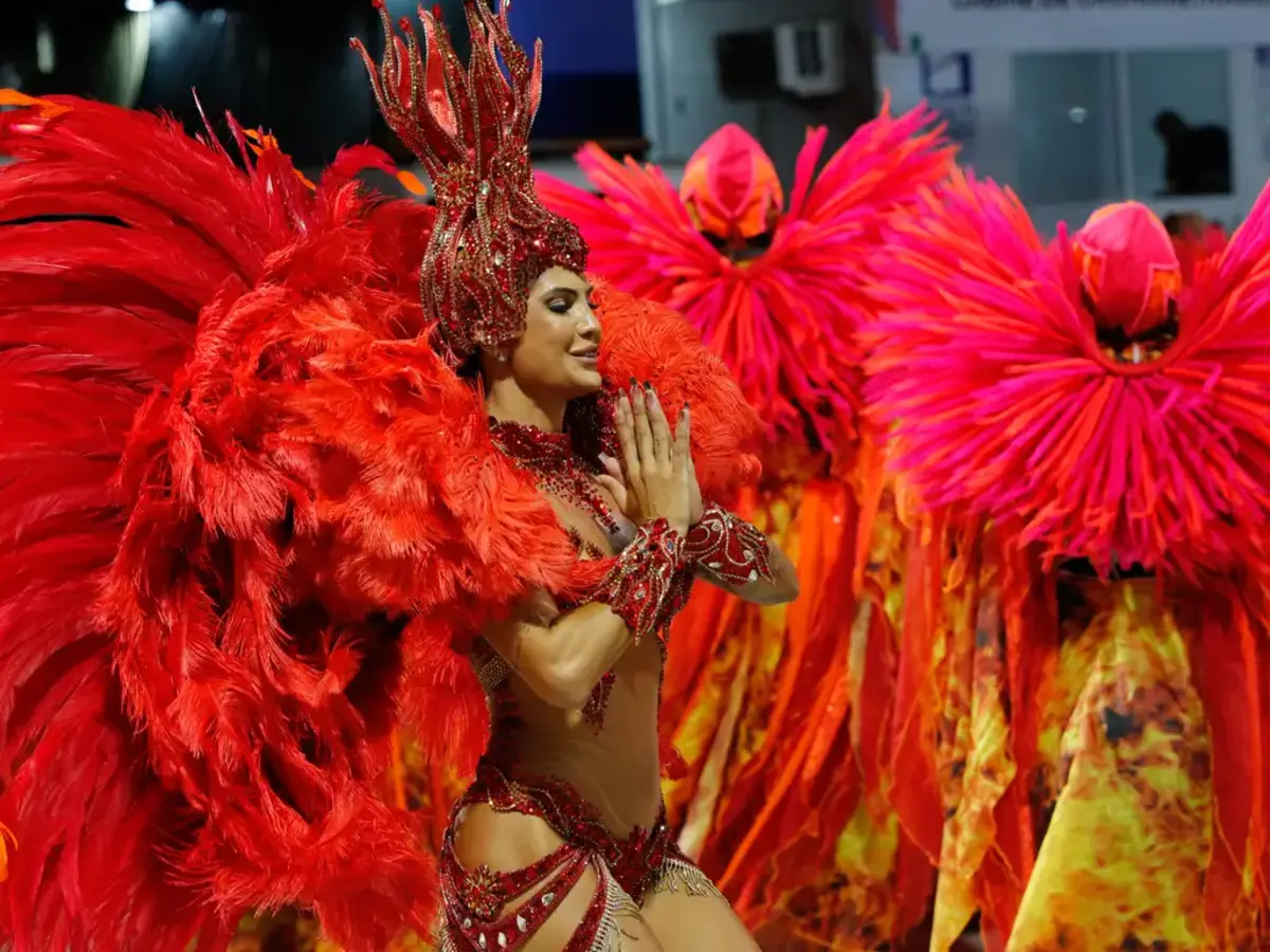 Mulher desfilando na escola de samba de vermelho, com plumas em vermelho.