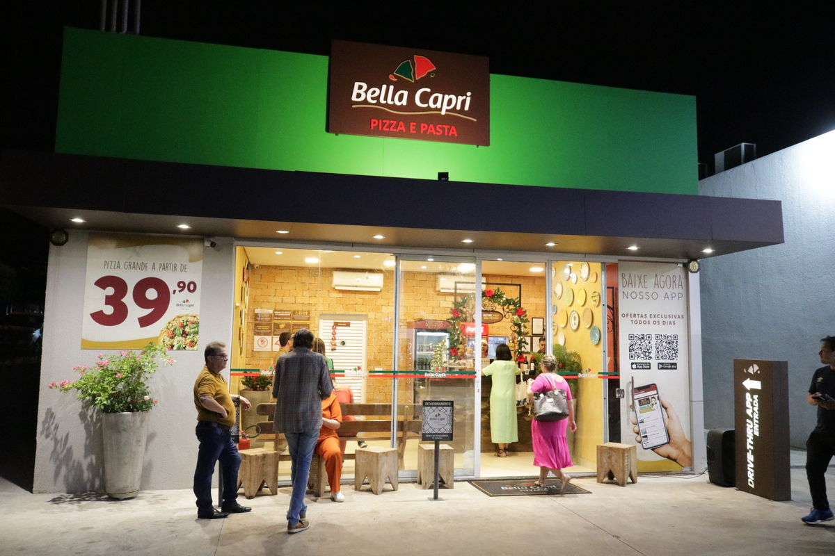 Fachada de loja da pizzaria da Bella Capri com clientes na porta.