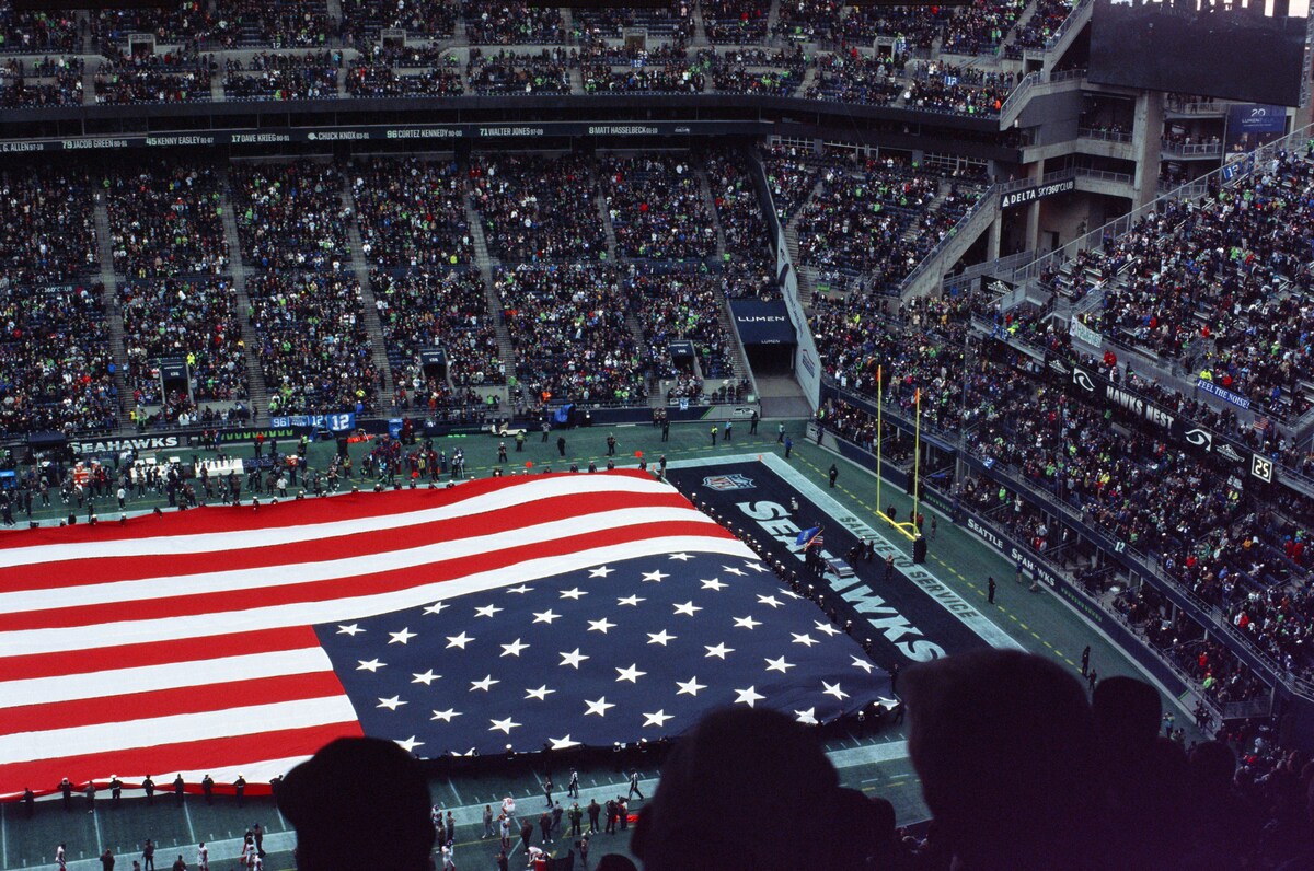 Visto de cima, estádio com plateias lotadas e, no lugar do campo, uma bandeira gigante dos Estados Unidos