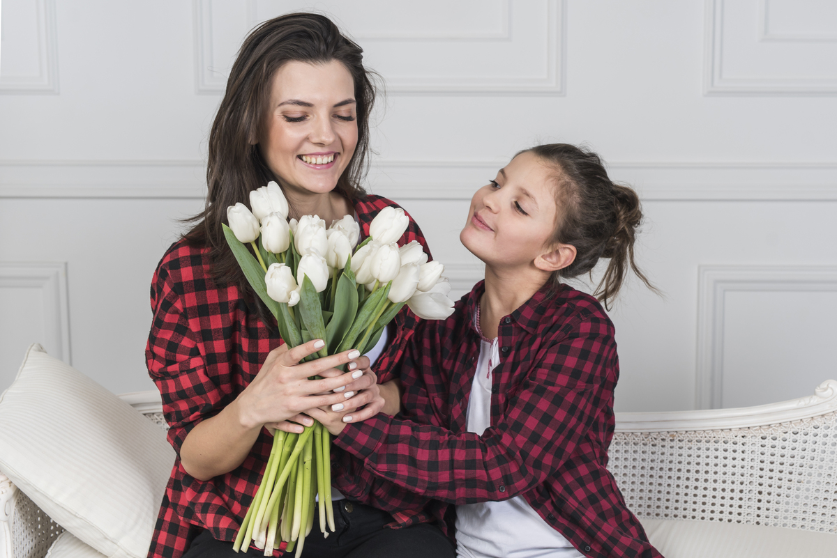 Menina presenteando mãe com flores no dia das mães. As duas usam camisas xadrez vermelhas iguais