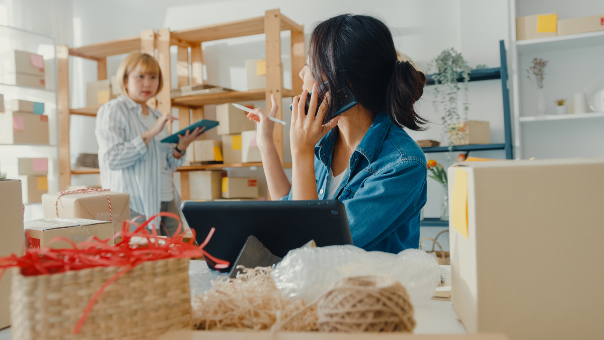 Jovens empresárias da Ásia usando chamadas de celular recebendo pedidos de compra e verificando o produto em estoque trabalham no escritório doméstico. Proprietário de pequena empresa, entrega no mercado on-line, conceito freelance de estilo de vida.