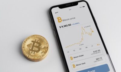 Celular com página de Bitcoin aberta, com moeda com "B" talhado ao lado; criptomoeda