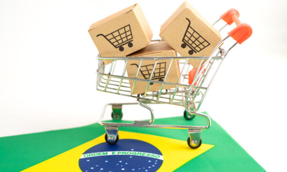 Carrinho virtual de supermercado cheio de caixas de compras, em cima de uma bandeira do Brasil ilustra investimentos no varejo brasileiro.