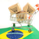 Carrinho de supermercado cheio de caixas de compras, em cima de uma bandeira do Brasil ilustra investimentos no varejo brasileiro.