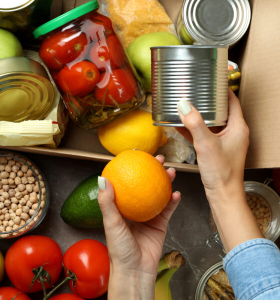 Mão feminina separa alimentos diversos e os coloca em caixa de doação, ilustrando a notícia de que a Connecting Food distribuiu mais de 48 toneladas de alimentos