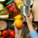 Mão feminina separa alimentos diversos e os coloca em caixa de doação, ilustrando a notícia de que a Connecting Food distribuiu mais de 48 toneladas de alimentos