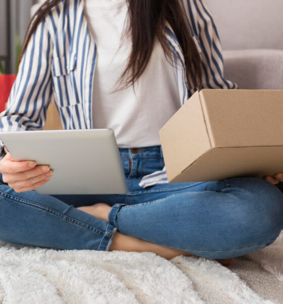 Mulher jovem com tablet e pacote nas mãos, sentada em casa. c-commerce