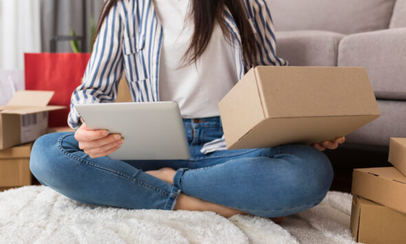 Mulher jovem com tablet e pacote nas mãos, sentada em casa. c-commerce