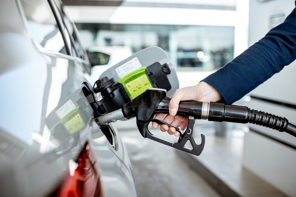 Homem reabastecendo carro com bomba de posto de gasolina.
