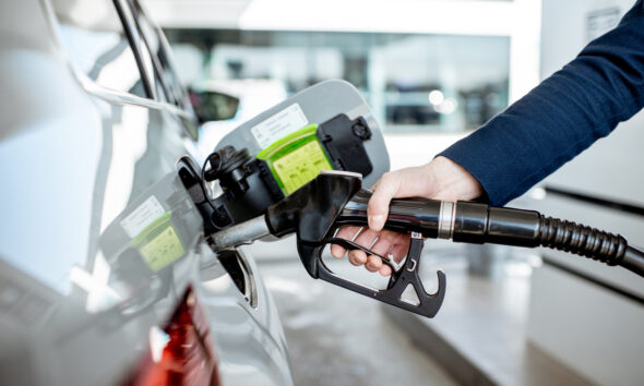 Homem reabastecendo carro com bomba de posto de gasolina.