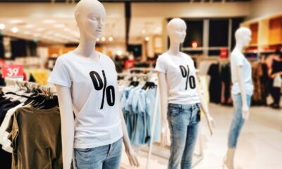 Dois manequins femininos com camiseta branca e símbolo de porcentagem e calça jeans, em fundo de loja de roupas.