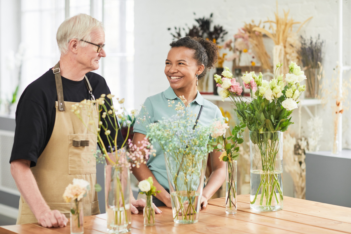 Homem de cabelo branco sorri para mulher negra atrás de vasos de plantas, ilustrando a tendência de humanização no varejo 5.0.
