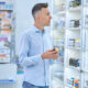 Homem branco de camisa e cabelo grisalho escolhe medicamentos em farmácia