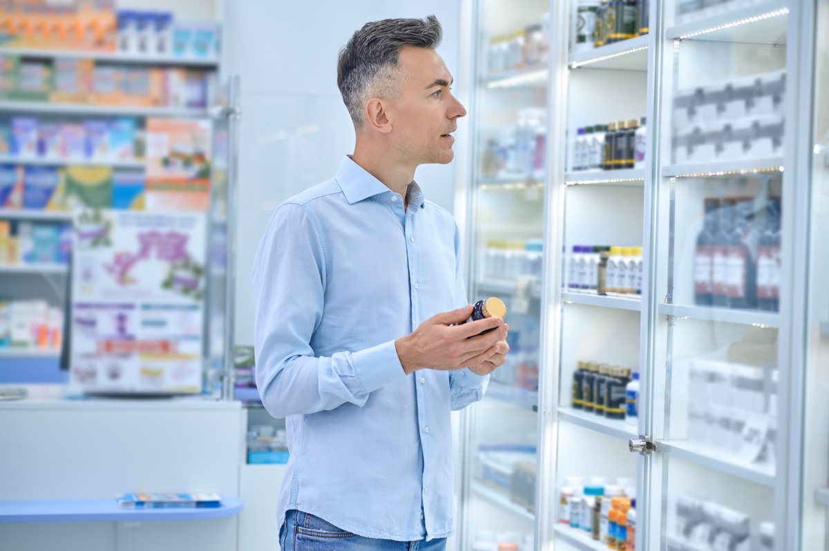 Homem branco de camisa e cabelo grisalho escolhe medicamentos em farmácia