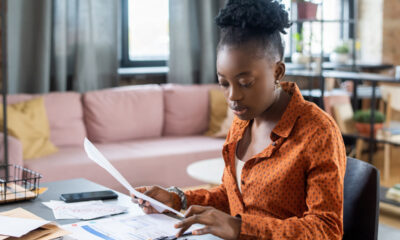 Mulher negra sentada à mesa calculando impostos a pagar; regularização de dívidas