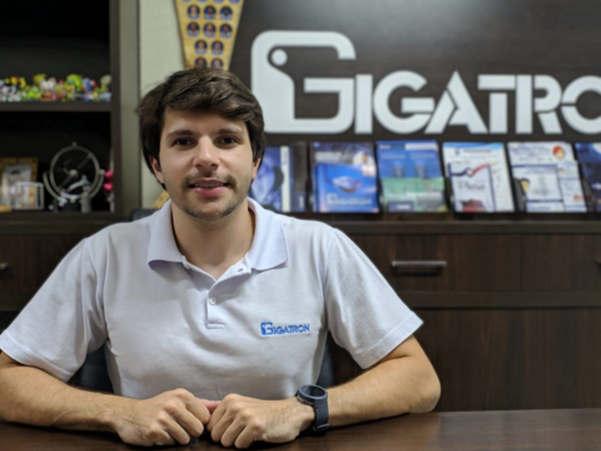 Victor Ruiz se posiciona à mesa, à frente de uma parede com logo da Gigatron