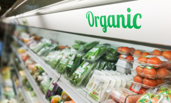 Área orgânica do supermercado, com legumes e frutas, e letreiro, em verde, escrito "Organic"; tarifaço