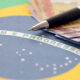 Close em bandeira do Brasil com cédulas de dinheiro em reais e caneta por cima; PIB; Focus