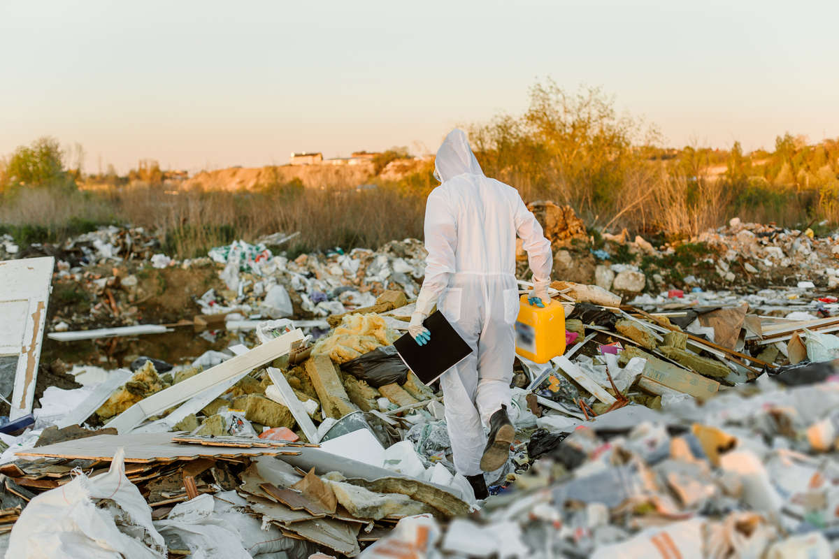 Pessoa com roupa de proteção de costas colhendo materiais em local cheio de escombros; eventos climáticos