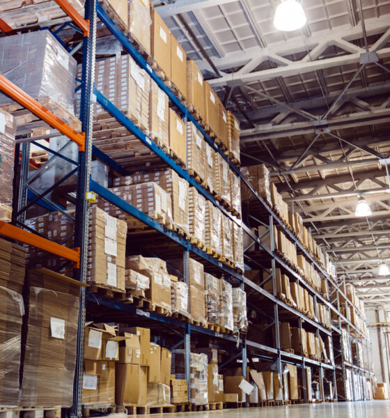 Prateleiras altas cheias de caixas em galpão, remetendo à logistica; frete; de minimis