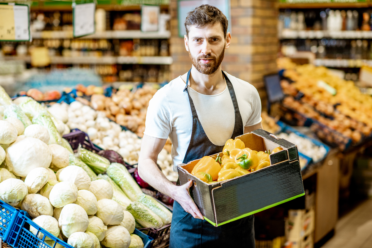 Trabalhador de supermercado segurando caixa com legumes; Ranking IBEVAR-FIA mostra crescimento do setor