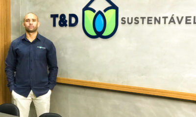 Camillo Torquato fica de pé à frente de logomarca da sua empresa, T&D Sustentável