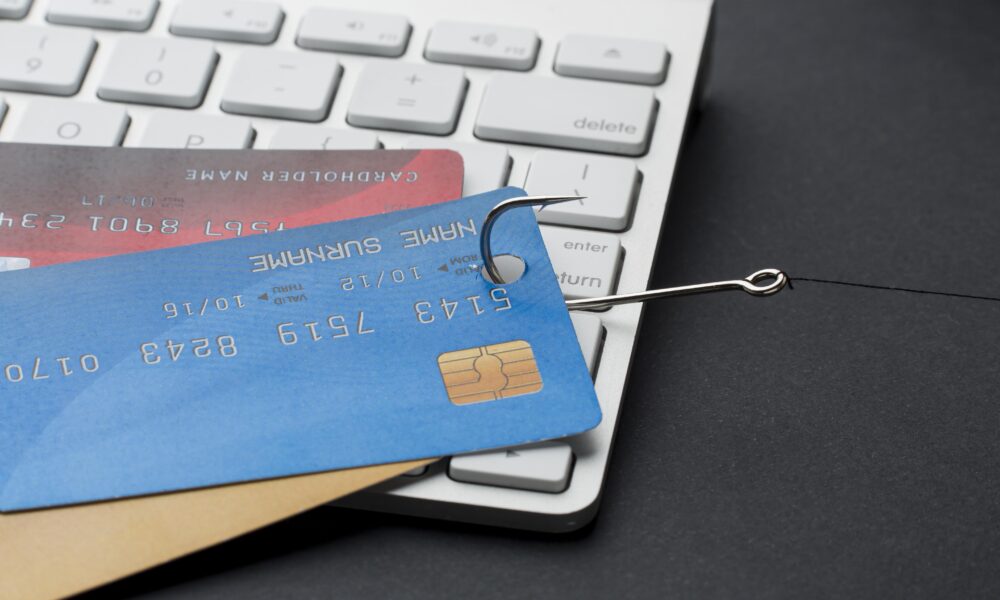 Anzol puxando cartões de crédito em cima de teclado de computador representando fraudes no e-commerce