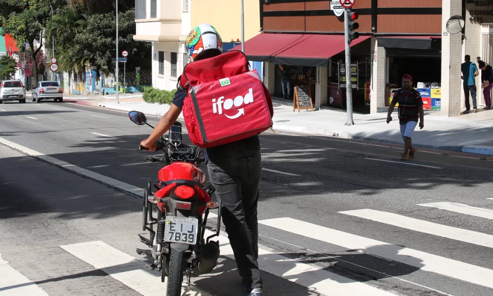 trabalhador de plataformas digitais na rua da consolação, em são paulo, guiando uma motocicleta e trajando uma mochila térmica de empresa de entregas rápidas