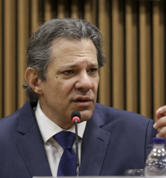 Fernando Haddad de terno, sentado, ao microfone, gesticulando; IOF