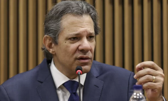 Fernando Haddad de terno, sentado, ao microfone, gesticulando; IOF