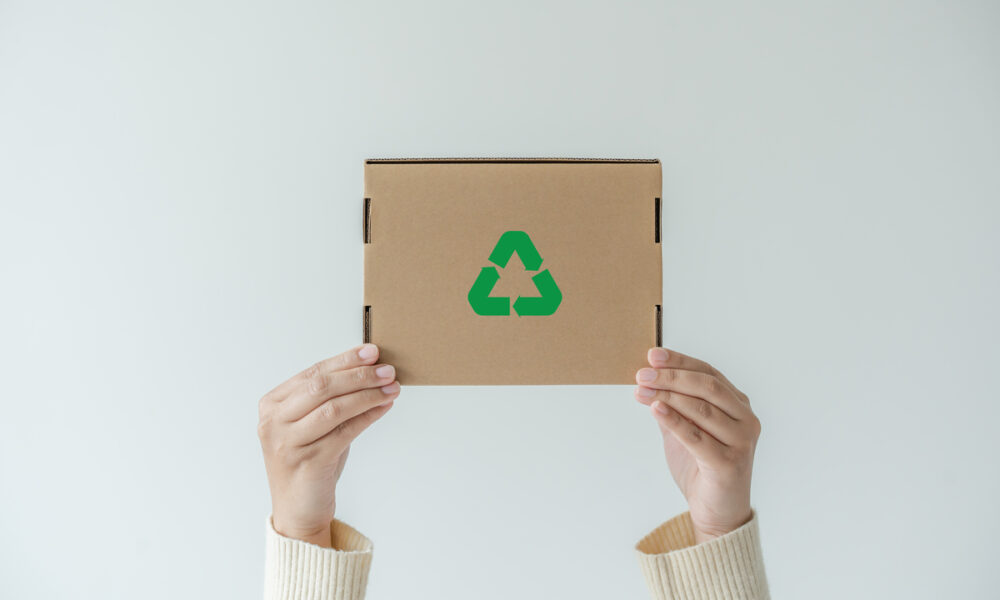 Mãos levantando uma caixa de papelão com símbolo verde de sustentabilidade