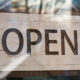 Placa de madeira atrás de vidro de estabelecimento escrita "Open"; canais de venda; IODE-PMEs