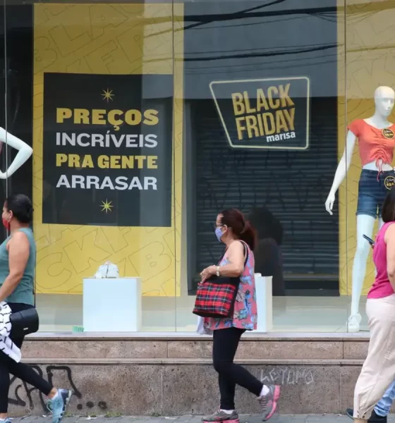 Pessoas passando em frente a loja de roupas, em promoção de Black Friday anunciada na vitrine; varejo