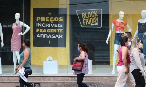 Pessoas passando em frente a loja de roupas, em promoção de Black Friday anunciada na vitrine; varejo