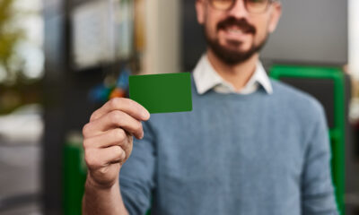 Foco suave do homem demonstrando cartão fidelidade verde em branco enquanto visitava posto de combustível durante o dia na cidade