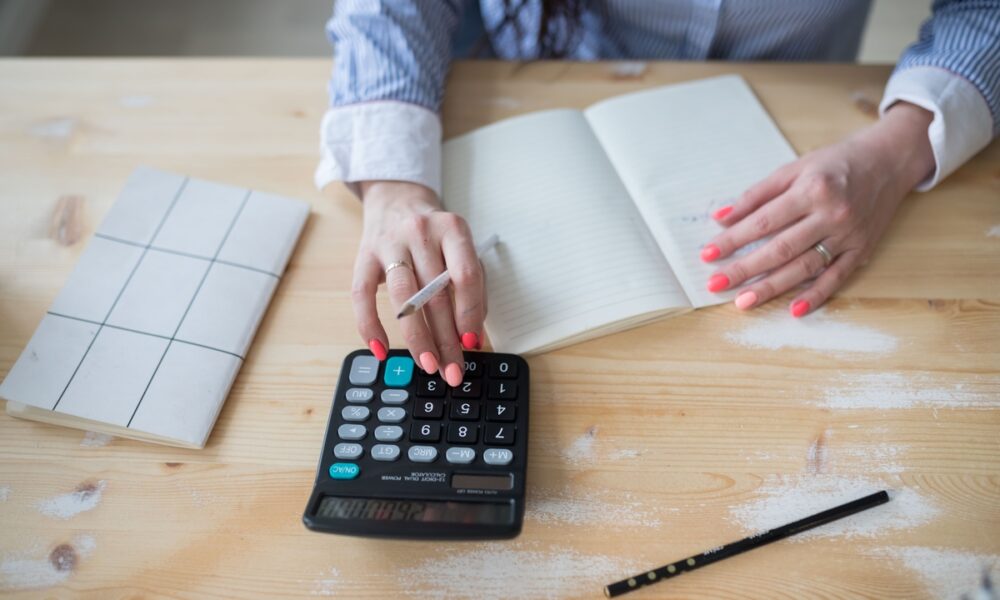 Mulher fazendo contas em calculadora e caderno