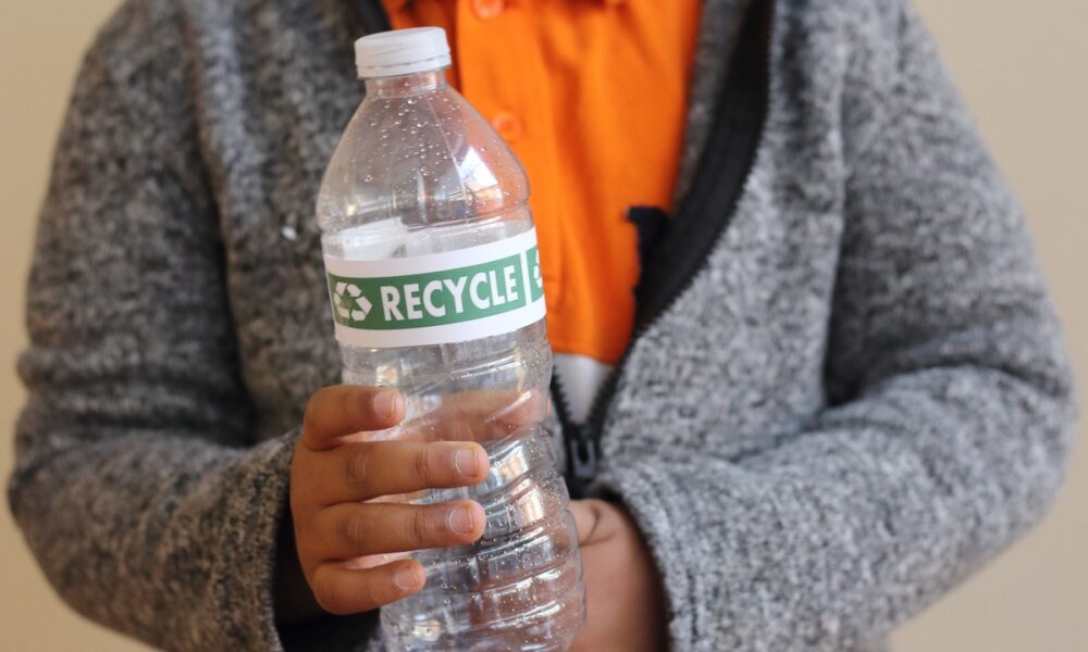 Pessoa com garrafa pet na mão com rótulo "recicle"