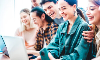 Cinco jovens sorrindo ao redor do computador, com a ideia de empreendedorismo social