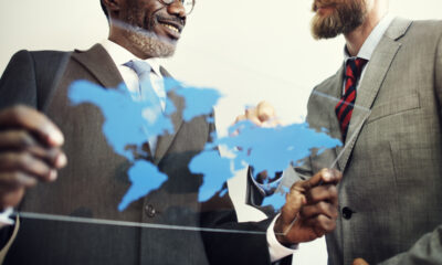 Dois CEOs - um negro e um branco - conversam segurando uma placa de vidro com mapa mundi em azul