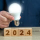 Empresário segurando lâmpada acesa em cima de bloquinhos com 2024 escrito