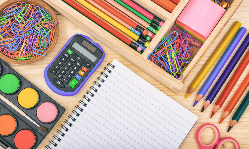 Material escolar organizado (caderno, calculadora, lápis, clips, tezoura, tinta de aquarela) lembra volta às aulas