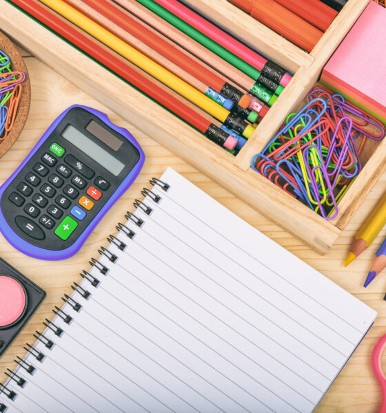 Material escolar organizado (caderno, calculadora, lápis, clips, tezoura, tinta de aquarela) lembra volta às aulas